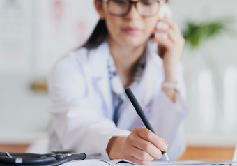 Médica escrevendo em um caderno enquanto fala ao telefone.