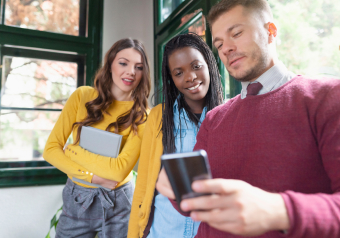 Três pessoas olhando um smartphone e discutindo algo juntos.