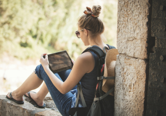 Mulher com mochila sentada ao ar livre usando um tablet."