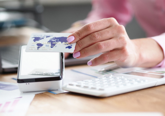 Pessoa segurando um cartão bancário próximo a uma máquina de pagamento digital.