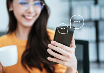Mulher sorridente segurando um smartphone, interagindo em um chat enquanto toma café.